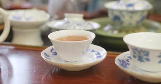 Close up of hands pouring tea from the pitcher into a tea cup. Gong fu cha session, a traditional chinese tea discipline. High dynamic range professional footage.