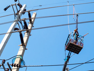 The electrician is working on the crane and the power lines on the blue sky background.