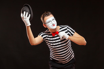Portrait of male mime artist performing, isolated on black background. Man raises his hat and...