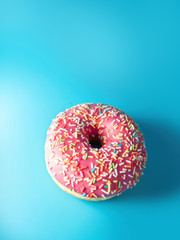 round pink berry doughnut with sprinkles on a blue background with a bright light