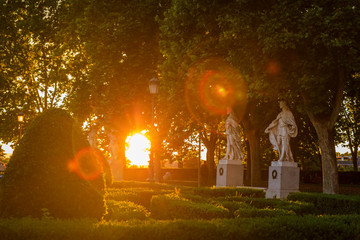 Sunset by Royal Palace or Palacio Real with Plaza de Oriente park statues and sun flares through the trees, Madrid Spain
