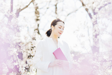 Obraz na płótnie Canvas 満開の桜の中で読書をする女性