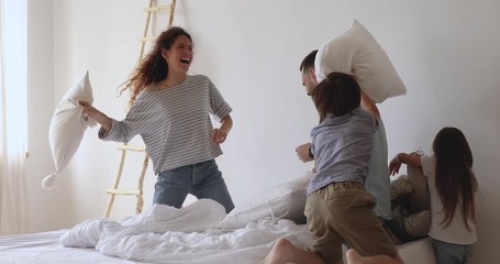 Happy playful family of four parents and little cute kids having fun pillow fight on bed, carefree couple with small funny small children laughing playing leisure game in bedroom on weekend together - Powered by Adobe