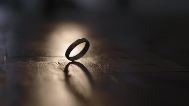 A Ring Whirling Slowly On Top Of The Wooden Table Inside A Dark Room With Little Ray Of Light - Closeup Shot