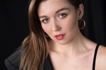 Attractive young woman in earrings looking at camera on black background