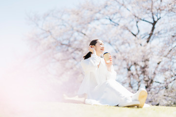 満開の桜の中、公園で珈琲を飲むミドル女性