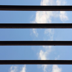 Fototapeta premium Blue sky with clouds, view through grating horizontal iron bars - self-isolation concept blank for text, quarantine, remote work from home