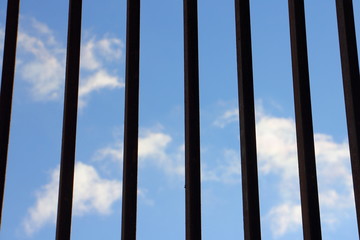 Blue sky with clouds, view through grating vertical iron bars - self-isolation concept, quarantine, office work from home