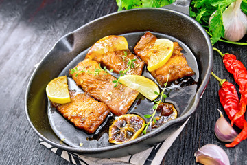 Salmon with sauce in pan on dark board