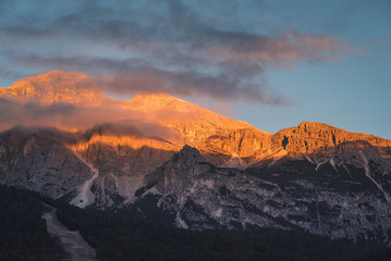 Naklejka na ściany i meble Morning sunlight illuminating the rocky mountain peaks of The Dolomites mountain ranges at sunrise. A scenic view taken from the town of Cortina in Italy