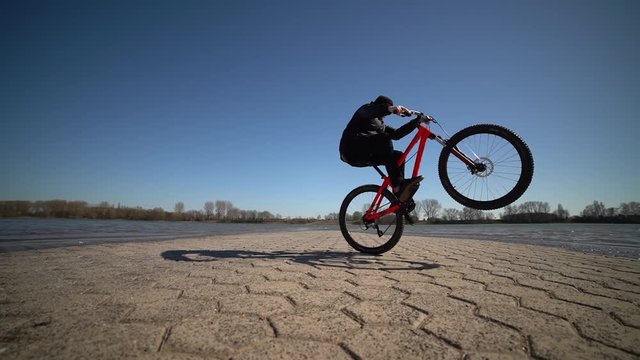 Spectacular Mountain Bike Wheelie In Slowmo Next To A River / Outdoor Sports / Blue Sky & Sunshine