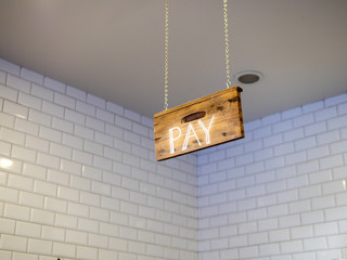 Wooden pay sign hanging over cash register payment area in cafe