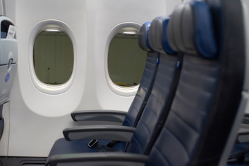 Airplane windows with blurry blue leather seats in foreground.