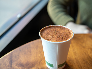 Coffee latte covered in cocoa powder in compostable cup on table in cafe