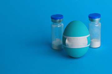 An Easter blue egg in medicine protective mask with two bottles of antibiotics behind. Blue background. Copy space. Easter on coronavirus COVID-19 quarantine. Monochrome Easter 2020. Stop VIRUS