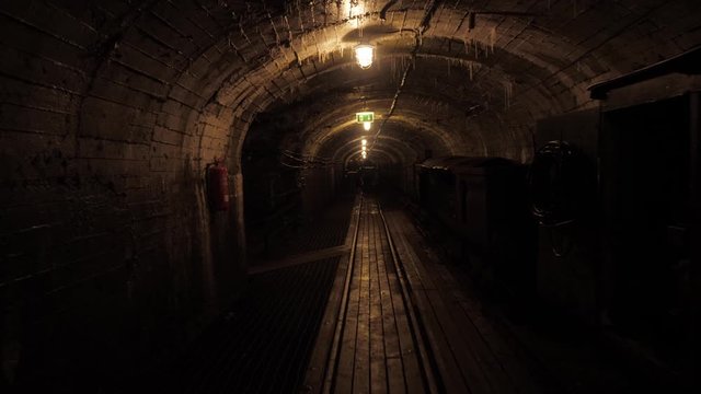 poorly lit wet damp mine tunnel with rails on the floor and a train trolley