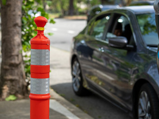 Skinny orange safety cone on sidewalk near street parking cars