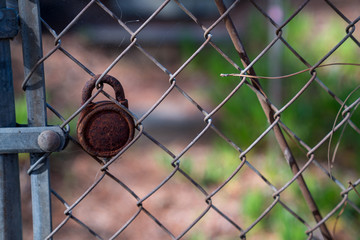 Rusted padlock hanging on fence in outdoor area on chain link fence