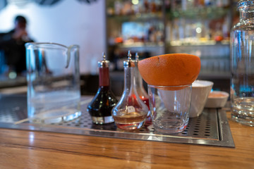 Half an orange sitting in a glass next to various cocktail and drink tools on bar counter