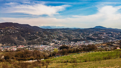 Fototapeta na wymiar Top view of the outskirts of the city and beautiful mountains under a blue cloudy sky in sunny weather. The Black Sea coast of the Caucasus.