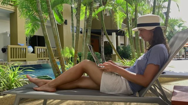 Busy freelancer woman smiling and working on laptop pc near swimming pool of luxury resort. businesswoman on vacation checking mail. concept hotel, browsing internet