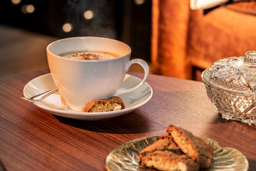 Eine Kaffeetasse mit gerösteten Kaffeebohnen auf einem hölzernenen Tisch. Sonneneinstrahlung, Reflexionen. Ein Cappuccino mit Milchschaum und Keksen. Serviert in einem Café. Milchkaffee
