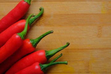 Close up shot of fresh red chilli pepper from top lay flat on yellow wood chopping board with copy space.