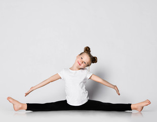 Smiling kid girl does gymnastic exercises at home splits with her arms outstretched and head tilted aside