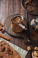 Turk with a wooden handle with cocoa, chocolate with a hot drink on a wooden table, cozy background, chocolate and cinnamon, a festive coffee shop. Place for text