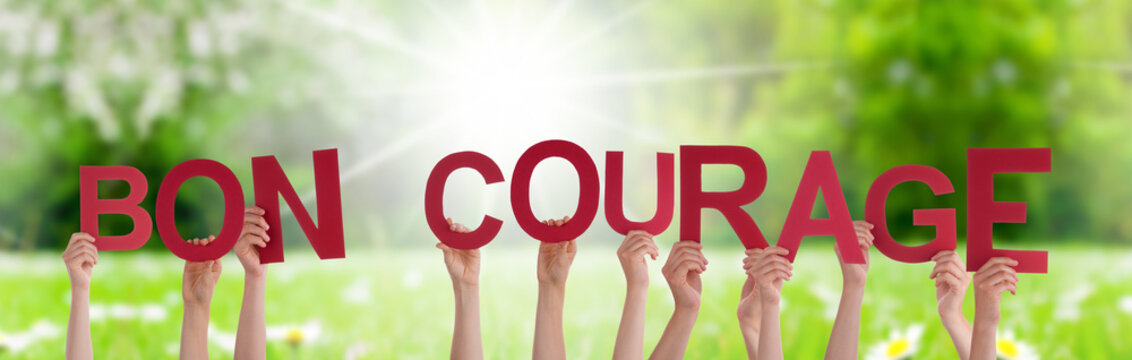 People Hands Holding Colorful French Word Bon Courage Means You Can Do It. Sunny Green Grass Meadow As Background