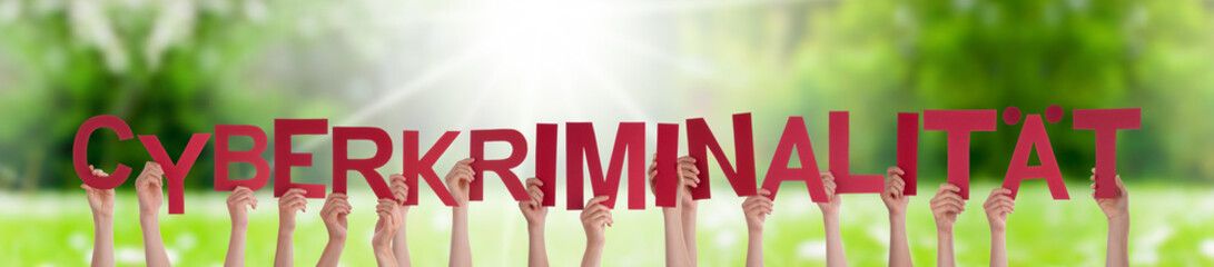 People Hands Holding Colorful German Word Cyberkriminalitaet Means Cyber Crime. Sunny Green Grass Meadow As Background