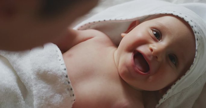 Authentic close up shot of a cute newborn baby in a white bathrobe is having fun with his mother after bathing and smiling. Concept of children,baby, parenthood, childhood, life, authenticity
