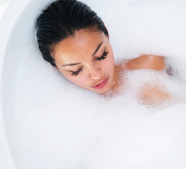 Top view portrait of beautiful and sensual brunette woman relaxing in bathtub with foam