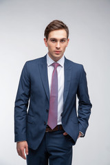 Fototapeta premium Young, handsome man in a blue suit in a white shirt with a tie on a white background in studio