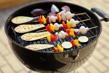 cooking, barbecue and food concept - close up of eggplant slices and vegetables with champignon mushrooms on bamboo skewers roasting on hot brazier grill outdoors