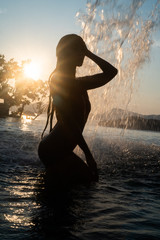 Silhouette of beautiful brunette woman in swimsuit posing in outdoor pool over sunset sky background