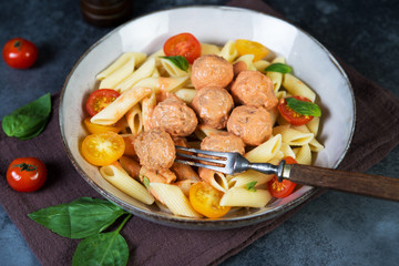 Penne pasta with meatballs tomatoes and sauce on a dark background