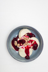 Cottage cheese pancakes or fritters with cherry sauce and chopped nuts on plain white background. Isolated. Healthy breakfast.