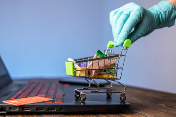 Hand in a sterile glove holds a shopping cart with a credit card. Internet purchasing during the coronavirus pandemic