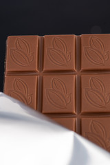 a bar of milk chocolate peeks out of an opened package on a dark background