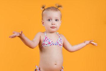 A little girl in a bright swimsuit spreads her arms to the sides