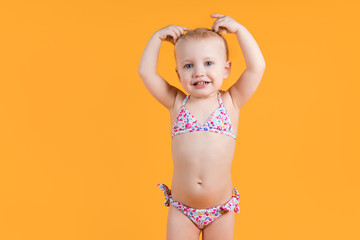 little girl in a swimsuit smiles and holds hands with ponytails on her head