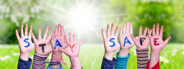 Kids Hands Holding Colorful English Word Stay Safe. Sunny Green Grass Meadow As Background