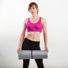 Sport woman holding a yoga or fitness mat while standing isolated over gray background