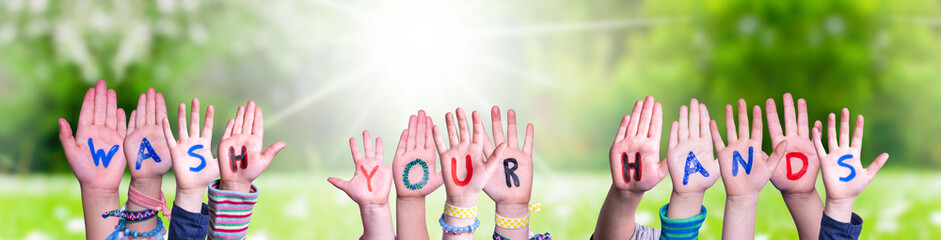 Kids Hands Holding Colorful English Word Wash Your Hands. Sunny Green Grass Meadow As Background