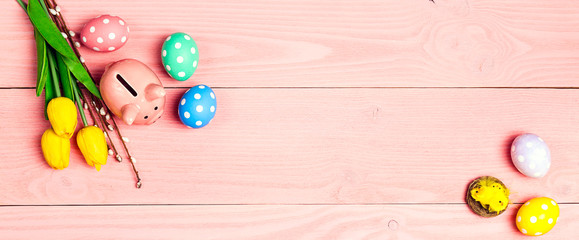 Piggy bank with eggs and tulip flowers on a pink wooden background. Saving money for easter holidays