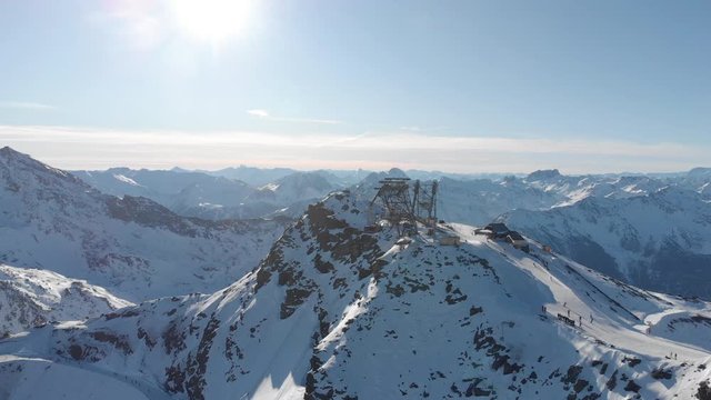 Orbit aerial over winter snowy mountain top ski tracks resort with skier people skiing. Drone video footage of Gondola lift cabin of ski-lift in the ski resort Val Thorens.