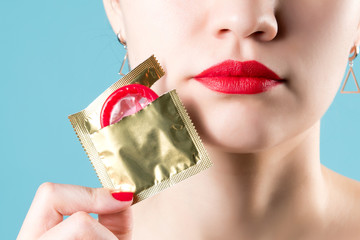 Close-up of a young girl's red lips and a red condom that peeks out of a package