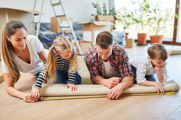 Eltern und zwei Kinder messen einen Teppich aus