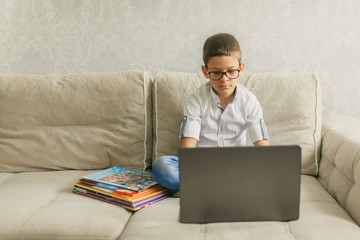 A schoolboy in glasses holding a video conference with a tutor on a laptop at home, sitting on the couch. The concept of distance learning.